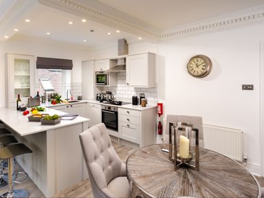 A kitchen and dining area with a round wooden table and cushioned chairs at Skyfall in Bowness