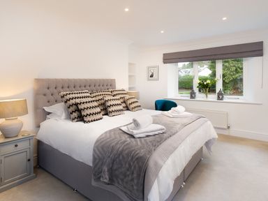 A bedroom with a bed with patterned pillows bedside tables and a window with a gray Roman blind at Skyfall in Bowness
