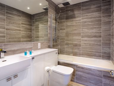 A bathroom with a sink, toilet, bathtub with shower, and brown tiled walls at Skyfall in Bowness