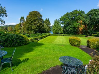 A garden with green grass shrubs and metal garden furniture at Skyfall in Bowness
