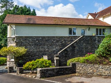 An exterior view of a stone and white stucco house with a tiled roof and surrounding greenery at Skyfall in Bowness
