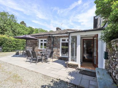A stone cottage with patio furniture and an umbrella outside at Rowan Cottage in Grasmere