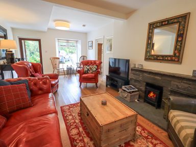 A living room with red leather sofas a wooden chest table a fireplace and a television at Rowan Cottage in Grasmere