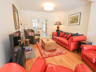 A living room with red leather sofas a wooden coffee table and glass doors at Rowan Cottage in Grasmere