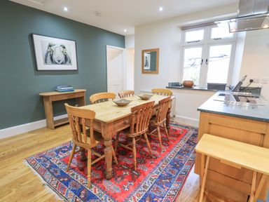 A dining area with a wooden table and six chairs on a red patterned rug at Rowan Cottage in Grasmere