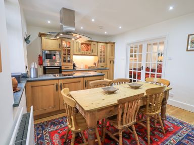 A kitchen with wooden cabinets dining table and chairs on a red patterned rug at Rowan Cottage in Grasmere