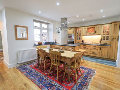 A kitchen with wooden cabinets and a dining table with six chairs on a patterned rug at Rowan Cottage in Grasmere
