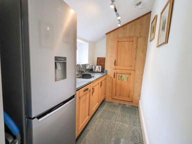 A kitchen with a refrigerator wooden cabinets a countertop with a sink and a toaster at Rowan Cottage in Grasmere