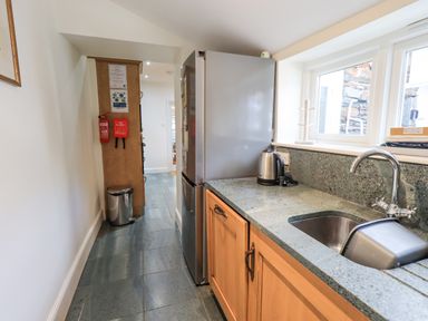 A narrow kitchen with a refrigerator countertop sink kettle and windows at Rowan Cottage in Grasmere