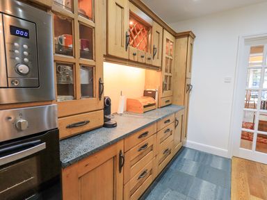A kitchen with wooden cabinets a granite countertop a built-in oven and microwave and a coffee machine at Rowan Cottage in Grasmere