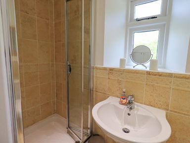 A bathroom with a shower enclosure and sink with a mirror and small window at Rowan Cottage in Grasmere