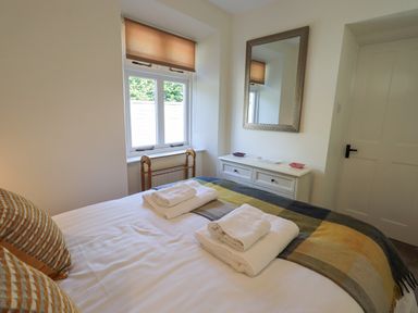 A bedroom with a bed covered in a striped blanket and folded towels a window dresser with a wall mirror and a white door at Rowan Cottage in Grasmere