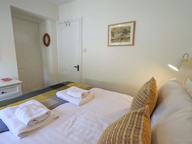 A bedroom with a bed with white and yellow pillows towels on the bed a bedside lamp and a painting on the wall at Rowan Cottage in Grasmere