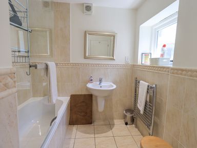 A bathroom with a bathtub a pedestal sink a mirror a towel rack and a window at Rowan Cottage in Grasmere