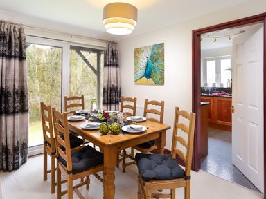 A dining room with a wooden table and six chairs next to sliding glass doors and a kitchen visible through an open door at Beech View in Ambleside