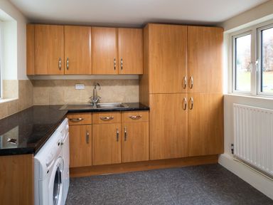 A kitchen with wooden cabinets a black countertop a sink a washing machine and a window at Beech View in Ambleside