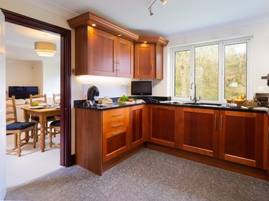 A kitchen with wooden cabinets black countertops a window over the sink and a dining area visible through a doorway at Beech View in Ambleside
