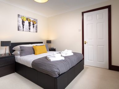 A bedroom with a bed with gray and white bedding and yellow pillow two bedside tables with lamps and a door at Beech View in Ambleside