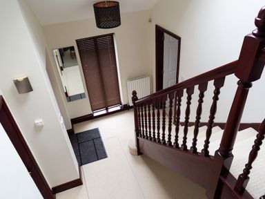 A staircase with wooden banister and beige carpet near a window with closed blinds in a hallway at Beech View in Ambleside