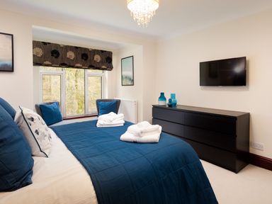 A bedroom with a blue bedspread window seats black dresser and a wall-mounted tv at Beech View in Ambleside