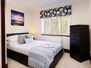 A bedroom with a bed a chest of drawers and a window with floral curtains at Beech View Ambleside