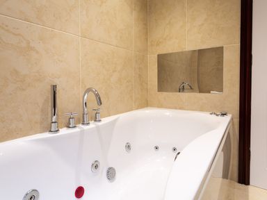 A corner bathtub with chrome faucets and beige tiled walls at Beech View in Ambleside