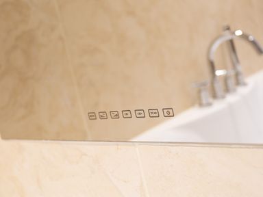 A bathroom mirror with digital control buttons and a bathtub faucet in the background at Beech View in Ambleside