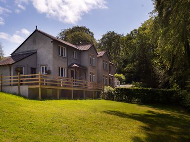 A house with multiple windows and a wooden fence on a grassy lawn surrounded by trees at Beech View in Ambleside