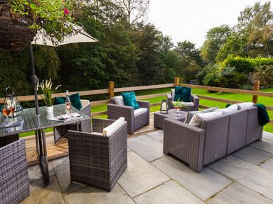 An outdoor patio with wicker furniture including chairs and a sofa with cushions and a table with drinks at Beech View in Ambleside
