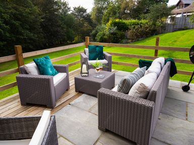 An outdoor patio with woven furniture including chairs and a sofa with cushions and a small table with drinks at Beech View in Ambleside