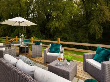 An outdoor patio with wicker chairs and tables with cushions and drinks surrounded by trees at Beech View in Ambleside