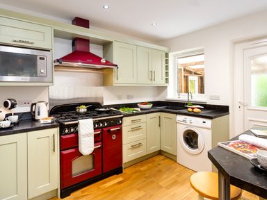 A kitchen with red stove and hood green cabinets washing machine and wooden floor at Artists Hideaway in Keswick