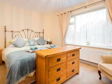 A bedroom with a bed sofa chair window with curtains and a wooden dresser at Artists Hideaway in Keswick