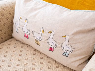 A cushion with embroidered ducks wearing colored boots on a patterned sofa at Artists Hideaway in Keswick