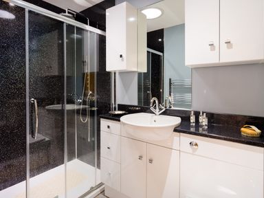 A bathroom with a shower enclosure a white sink and cabinets at Artists Hideaway Keswick