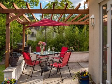 An outdoor patio with a glass table four red chairs and a red umbrella under a wooden pergola at Artists Hideaway Keswick