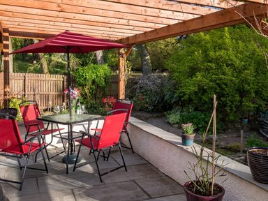 An outdoor patio with a glass table and red chairs under a wooden pergola at Artists Hideaway in Keswick