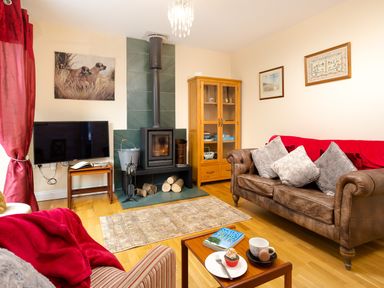 A living room with a brown sofa and a fireplace with stacked firewood at Artists Hideaway in Keswick
