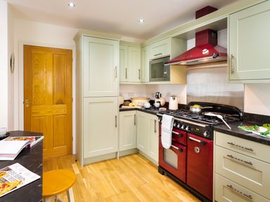 A kitchen with light green cabinets a red stove and wooden floor at Artists Hideaway Keswick
