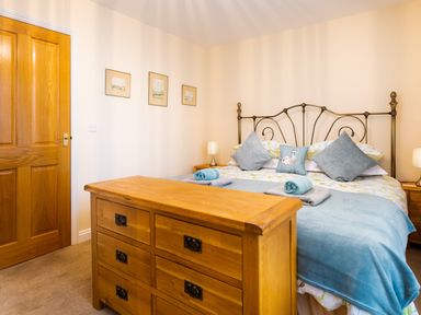 A bedroom with a wooden dresser wooden door and a bed with blue and floral bedding at Artists Hideaway Keswick