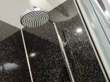 A showerhead with a chrome finish attached to a wall with black speckled tiles at Artists Hideaway in Keswick