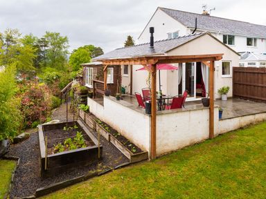A backyard with a raised garden bed a patio area with table and chairs under a wooden pergola at Artists Hideaway in Keswick