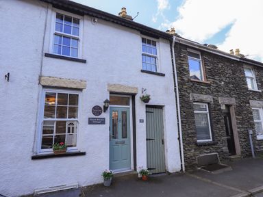 Front view of a white cottage with green door and windows with flowers at Tizzie Whizie Cottage in Windermere