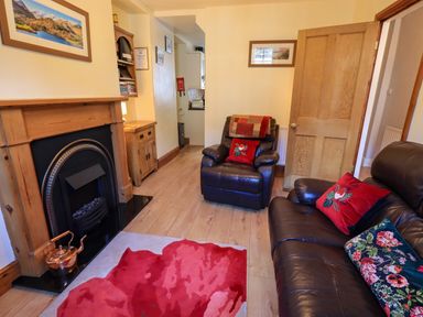 A living room with a fireplace wooden furniture two leather chairs and a sofa with cushions at Tizzie Whizie Cottage in Windermere