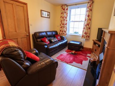 A sitting room with leather armchairs and sofa a floral rug and curtains near a window at Tizzie Whizie Cottage in Windermere