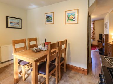 A dining area with a wooden table and four chairs next to a doorway leading to a living room at Tizzie Whizie Cottage in Windermere