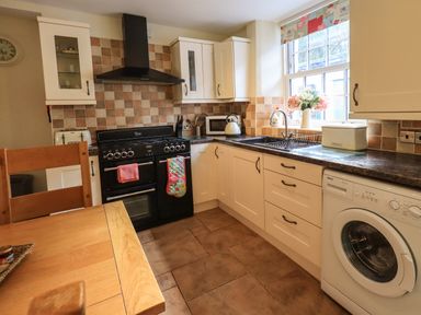 A kitchen with a stove washing machine sink and cabinets at Tizzie Whizie Cottage in Windermere