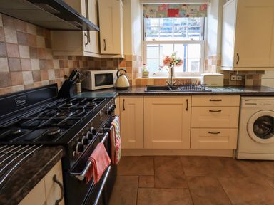 A kitchen with a gas stove microwave washing machine and a window above the sink at Tizzie Whizie Cottage in Windermere