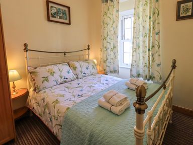 A bedroom with a double bed floral bedding bedside tables lamps and a window with floral curtains at Tizzie Whizie Cottage in Windermere