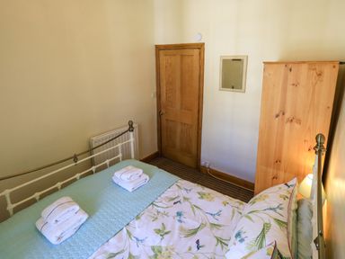 A bedroom with a bed made with floral bedding towels on a blue quilt a wooden door a wardrobe and a lamp at Tizzie Whizie Cottage in Windermere